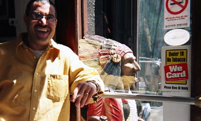 An Indigenous man posing next to a 'Cigar Store Indian' showing how harmful these representations are